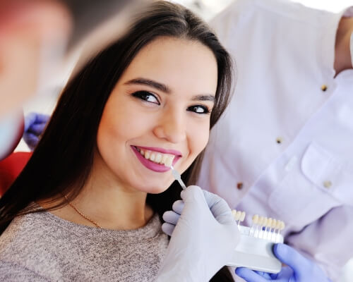 Dentist holding a veneer shade guide to a patients smile