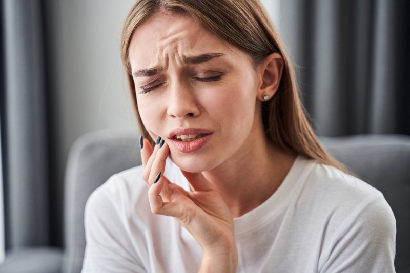 Woman holding her cheek while sitting in a chair and grimacing